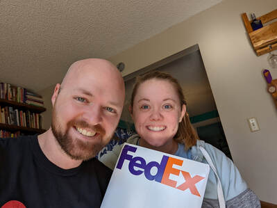 Robert and Rebecca are smiling, holding a big FedEx mailing envelope